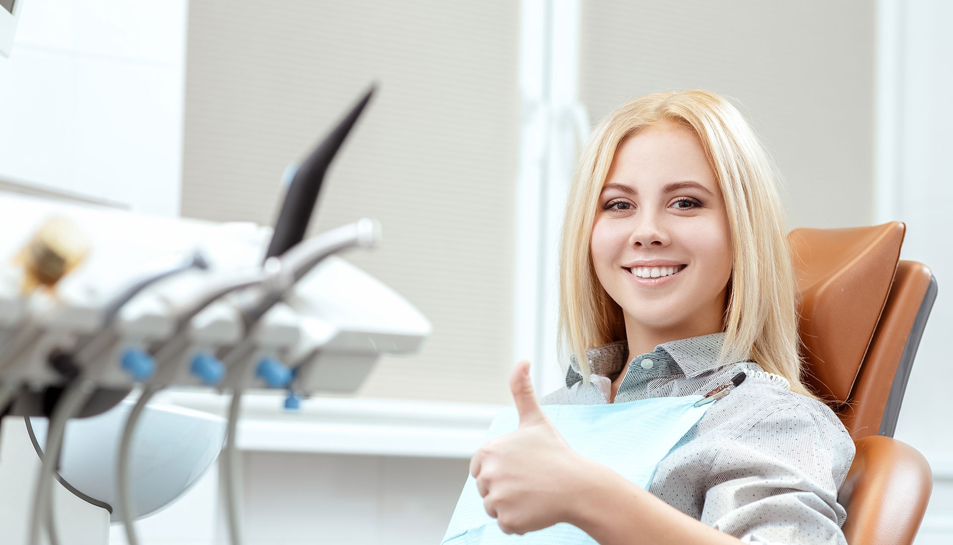 A woman in a dental chair, smiling and giving a thumbs-up.