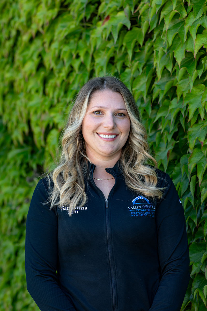 Woman in black jacket posing for photo with green ivy backdrop.