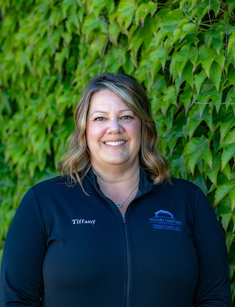 A woman standing outdoors, smiling and posing for the camera.