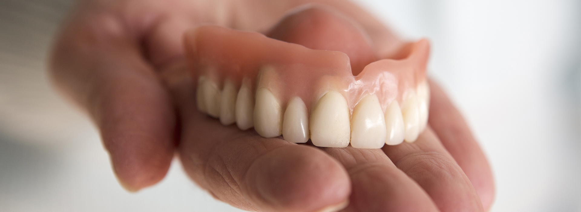 An individual is holding a set of artificial teeth with a natural tooth.