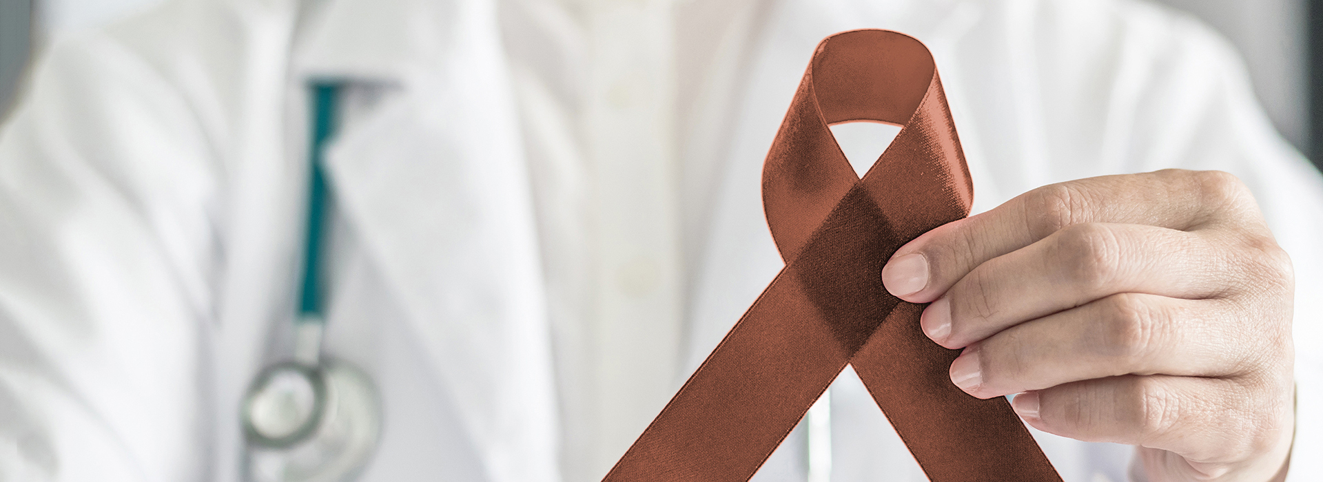 The image shows a medical professional holding up a red ribbon with a white cross, symbolizing the awareness of a specific health condition.
