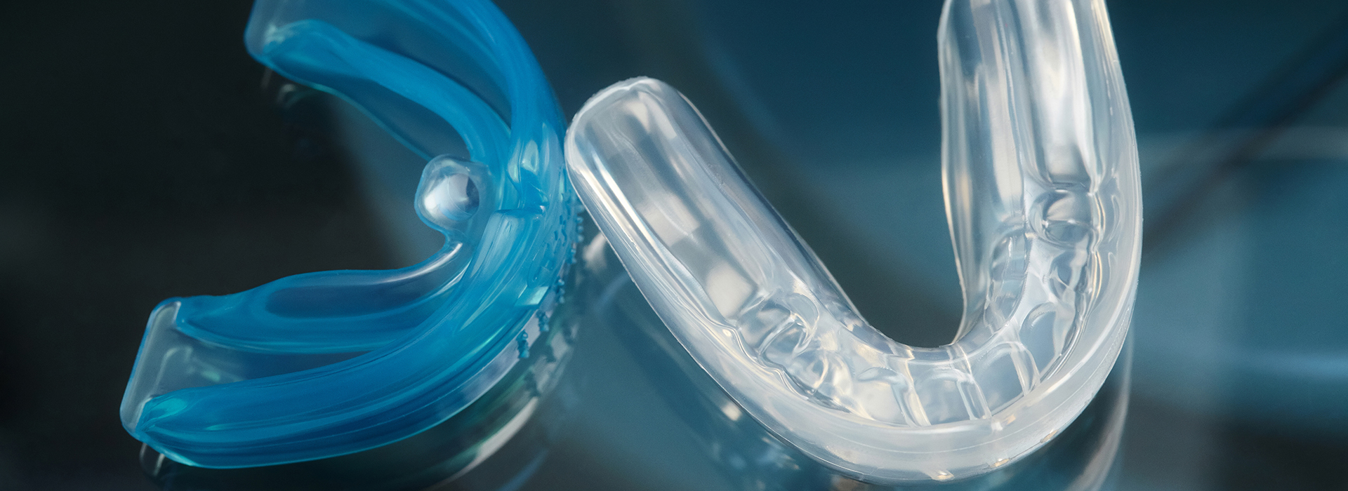 The image shows a close-up of a blue and clear plastic object with a curved shape, resembling a pair of glasses, against a blurred background.